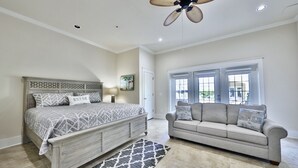 A bedroom with a bed, a gray sofa, a ceiling fan, and a window with blinds. - ECDI | PCB Near 30-A 5BR 4BA Pool Hot Tub EV Charger Early Booking Discounts (Panama City Beach)