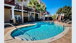 A swimming pool with a curved edge, surrounded by lounge chairs and palm trees. - ECDI | PCB Near 30-A 5BR 4BA Pool Hot Tub EV Charger Early Booking Discounts (Panama City Beach)