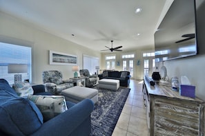 A spacious living room with a large ceiling fan, a flat-screen TV mounted on the wall, and a wooden cabinet with various items on top.