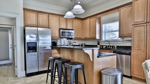Una cocina con armarios de madera, electrodomésticos de acero inoxidable, un espacio con taburetes de bar y una ventana con persianas.