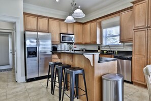 Una cocina con armarios de madera, electrodomésticos de acero inoxidable, un espacio con taburetes de bar y una ventana con persianas.