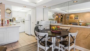 A modern kitchen with white cabinetry, a dining area with a round table and chairs, and a large mirror reflecting the kitchen. - 2nd Floor @ THE SUMMIT 1BR 1.5 BA  Free Beach Chairs!  $240 Weekly Value (Panama City Beach)