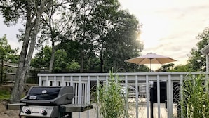 Una griglia barbecue su un patio con ringhiera bianca, circondato da alberi e un ombrellone.