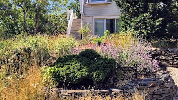 Una casa con una finestra a bovindo, circondata da un giardino ricco di piante e da un muro in pietra.