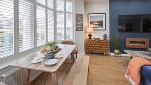 Een moderne woonkamer met een houten eettafel, banken, een bank en een aan de muur bevestigde televisie.