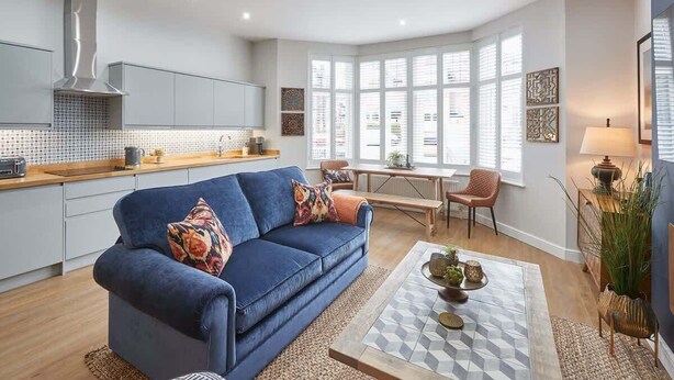 Een moderne keuken met grijze kastjes, een blauwe bank en een eethoek met een tafel en stoelen.