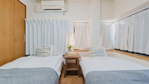 A hotel room with two beds, a wooden nightstand, a small table, and a window with curtains.