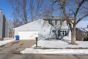 A single-story house with a garage, a tree in front, and a blue trash bin.
