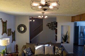 A living room with a sofa, decorative wall art, a staircase, and a kitchen area with a refrigerator.