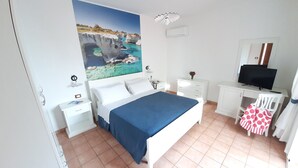 A bedroom with a bed, a desk, a TV, and a painting of a coastal scene. - Superior apartment with view and garden (Santa Maria di Leuca)