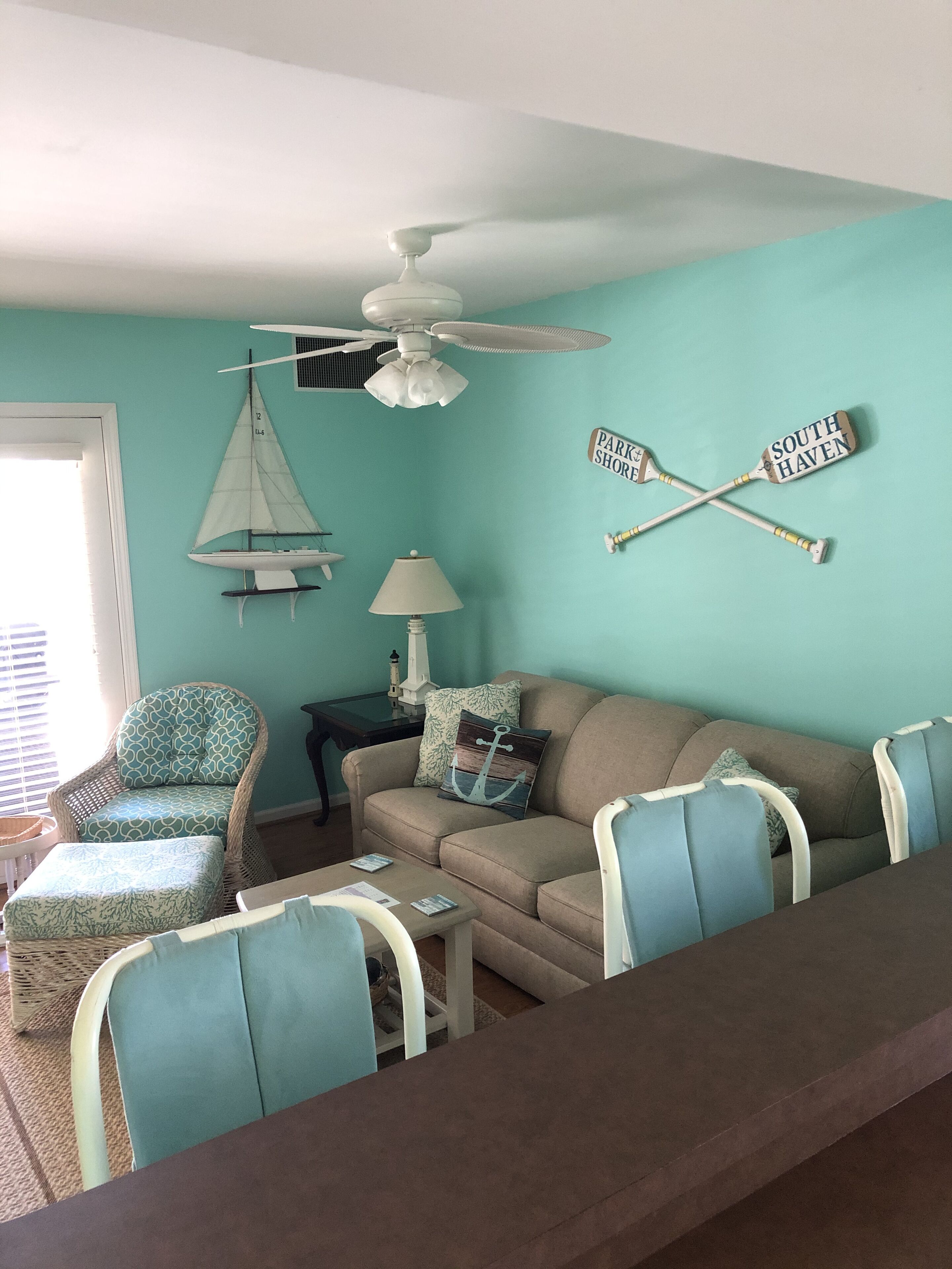 A living room with teal walls, a ceiling fan, a sailboat decoration, and two paddleboard signs.