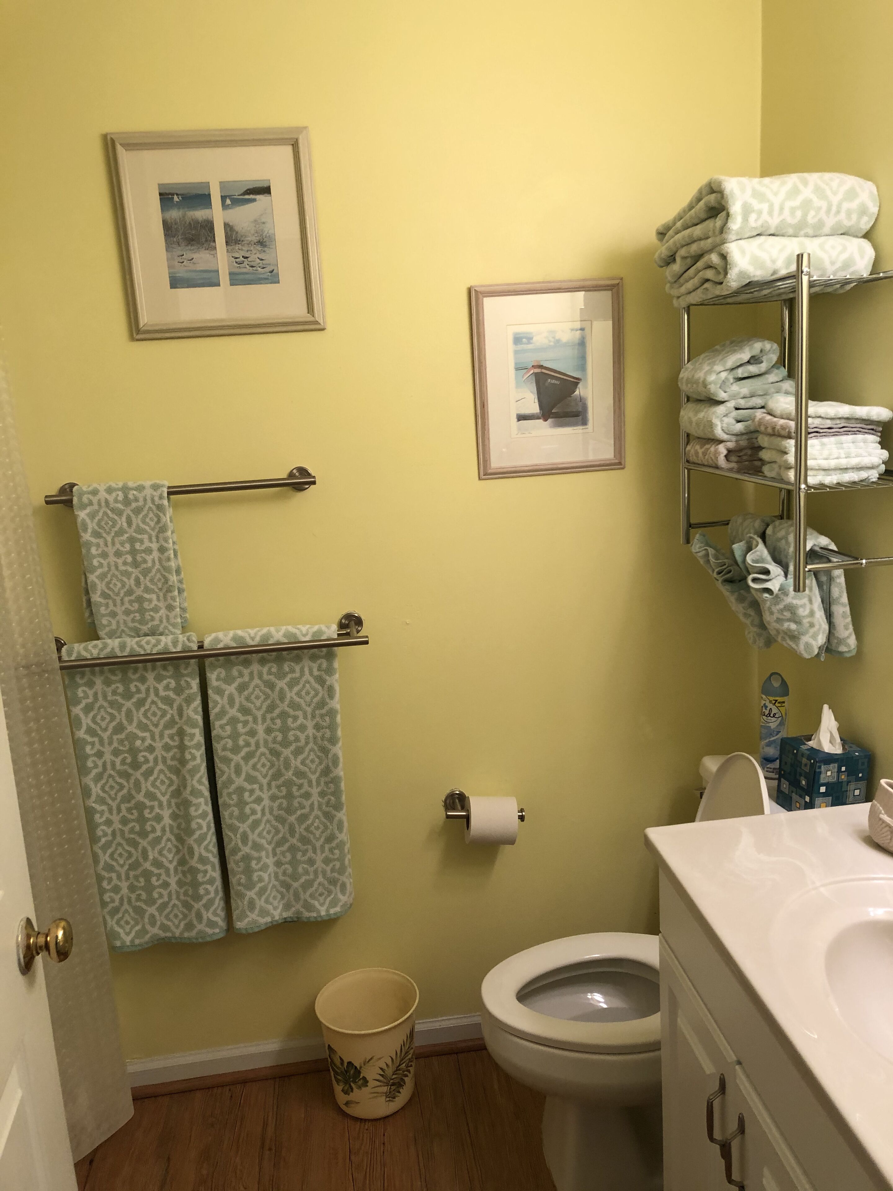 Un bagno con il water, un lavandino, un porta asciugamani con asciugamani decorati, un porta carta igienica e un quadro appeso al muro.