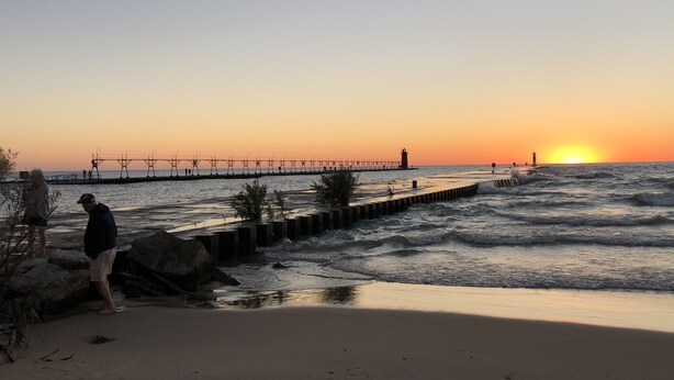 Una playa con un muelle que se adentra en el agua, un faro y una puesta de sol.