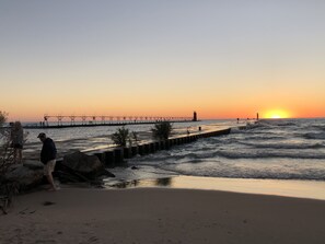 A beach with a pier extending into the water, a lighthouse, and a sunset. - South Haven - No Stairs - Condo with Pool - 2 minute Walk to Beach! (South Haven)