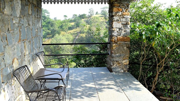 A balcony with stone walls, metal chairs, and a table. - The Sky Imperial Jungle Camp Resort (Kumbhalgarh)