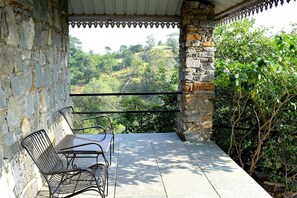 Un balcon avec des murs en pierre, des chaises en métal et une table.