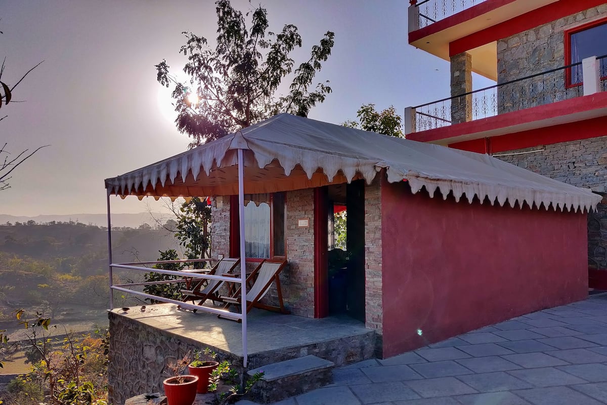 Il s’agit d’un petit bâtiment d’un seul étage, à la façade rouge et doté d’un auvent blanc. On y trouve un balcon avec deux chaises et une table, et des plantes en pot sont disposées au sol.