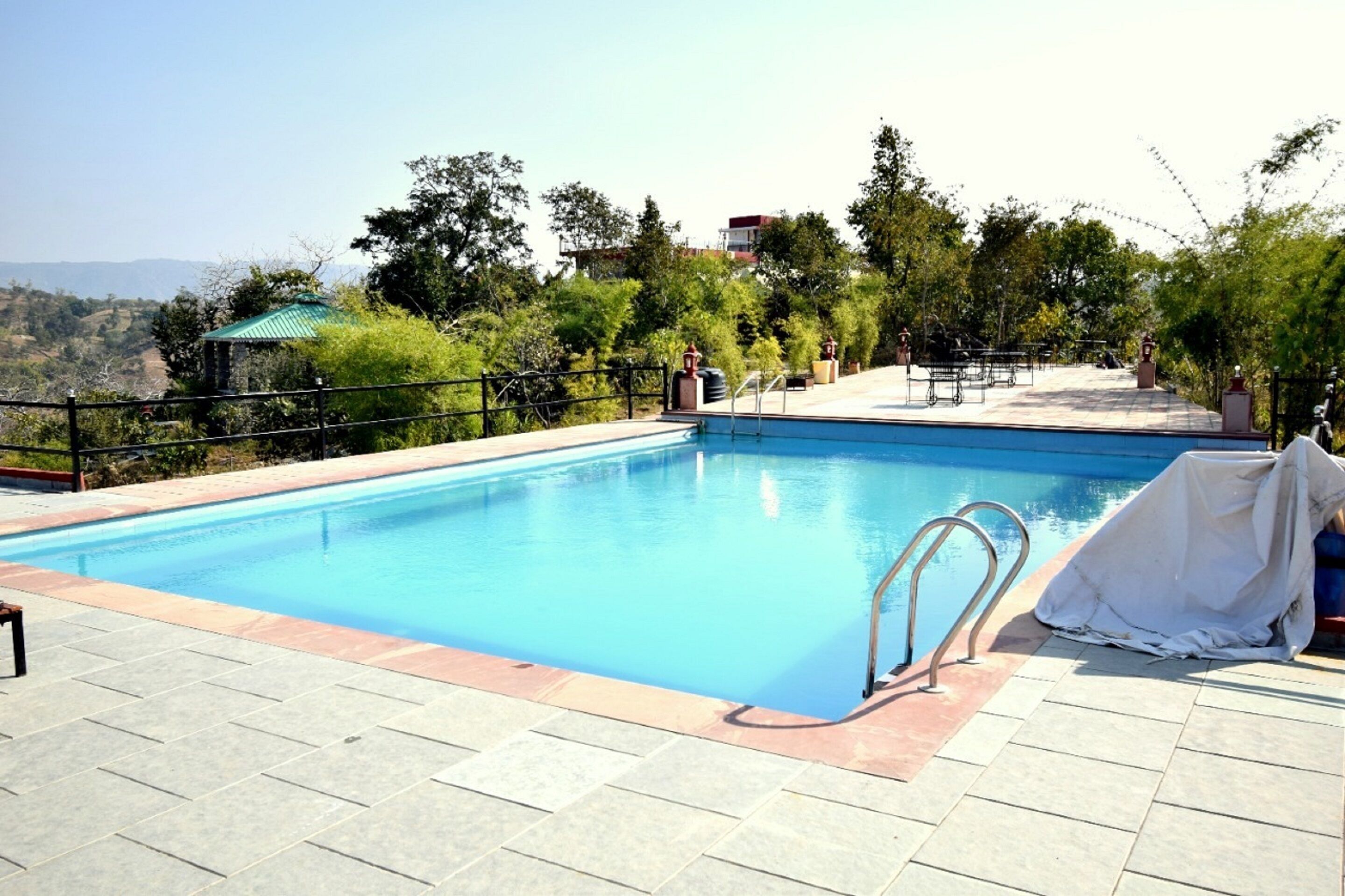 Une piscine avec un escalier en métal, entourée d’une terrasse carrelée et d’une clôture.