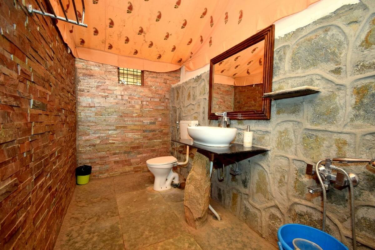 Une salle de bain avec un mur en briques, des toilettes blanches, un lavabo avec un miroir et une douche.