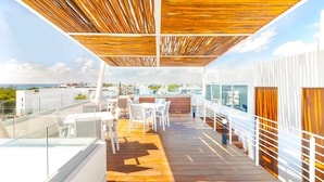 Une terrasse moderne sur le toit, dotée d’un plancher en bois, de mobilier blanc et de rampes en verre.