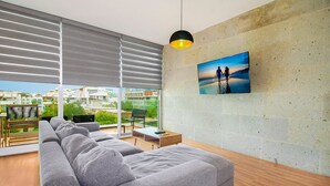 Un salon moderne avec un canapé d’angle gris, une table basse en bois et un tableau représentant un couple sur une plage.