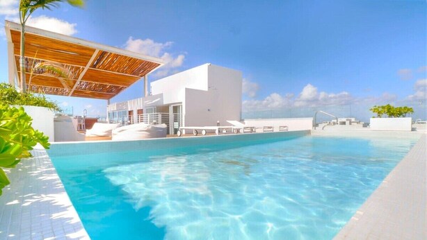 Une piscine à l’eau d’un bleu cristallin, un bâtiment blanc et une pergola en bois.