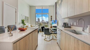 A modern kitchen with a central island, dining area, and large windows offering a city view. - One Bedroom Condo King Bed With City Views (Miami)
