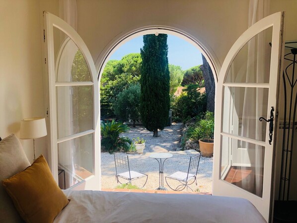 A bedroom with a large arched window leading to a garden.