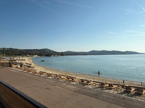 Una playa con sillones de madera y vistas al mar y colinas lejanas.