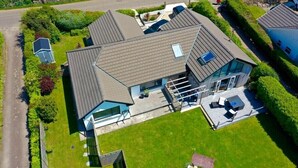 An aerial view of a modern two-story house with a sloped roof, a covered patio with outdoor furniture, and a swimming pool in the background. - Modern & Cosy Home with Hot-Tub, 5min drive to Beach, ideal for large families. (Goldsithney)
