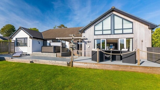 A modern two-story house with a large deck, a covered outdoor seating area, and a visible garage. - Modern & Cosy Home with Hot-Tub, 5min drive to Beach, ideal for large families. (Goldsithney)