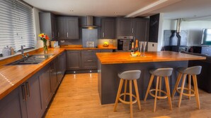 A modern kitchen with grey cabinets, a wooden countertop, and a central island with stools. - Modern & Cosy Home with Hot-Tub, 5min drive to Beach, ideal for large families. (Goldsithney)