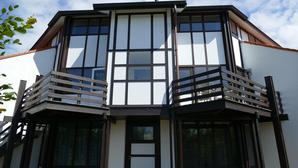 A multi-story building with a prominent corner balcony, large windows, and a white facade.