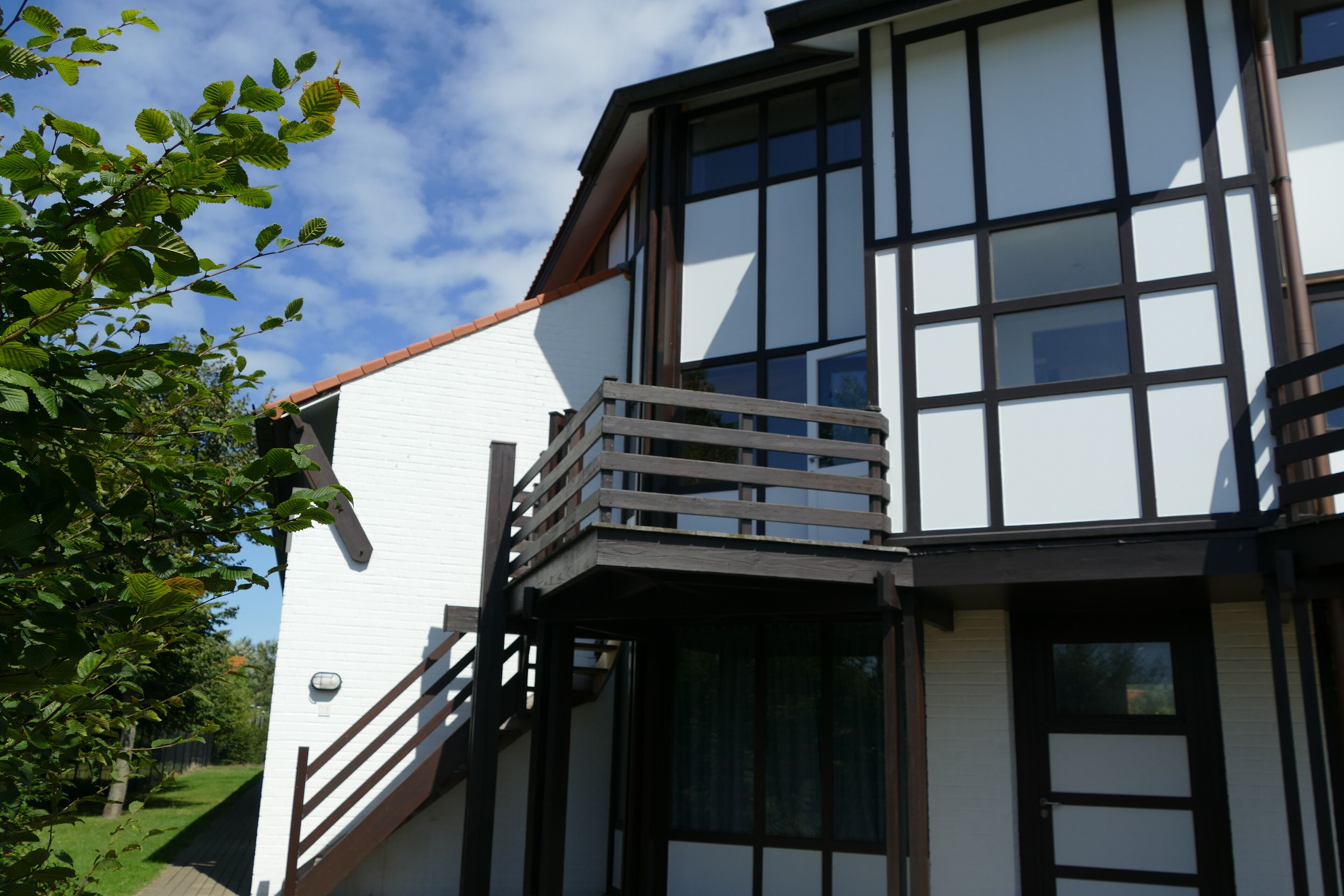A modern building with a white facade, large windows, and a wooden balcony.