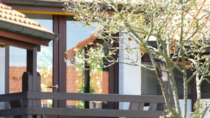 A wooden deck with a railing, a tree in the foreground, and a building with a tiled roof in the background.
