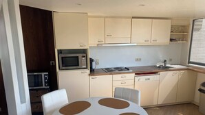 A compact kitchen with a microwave, stove, and dishwasher. There is a round table with chairs in the center.