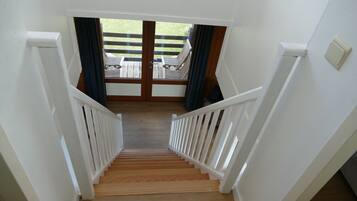 A wooden staircase with white railings leading to a balcony with a view of a grassy area and outdoor furniture.