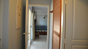 A narrow hallway leading to a bedroom with a bed, a nightstand, and a lamp.