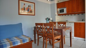 A dining area with a wooden table and chairs, a blue sofa, and a kitchen with wooden cabinets and a microwave.