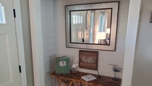 A wooden console table with a mirror above it, a 'hello' sign, and a small plant.