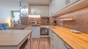 A compact kitchen with white cabinets, a wooden countertop, a microwave, a dishwasher, and a coffee machine. - La Brigantine - appartement avec piscine proche plage (Gruissan)