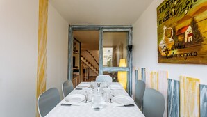 A dining area with a table set for four, chairs, a chandelier, and a painting on the wall. - La Brigantine - appartement avec piscine proche plage (Gruissan)