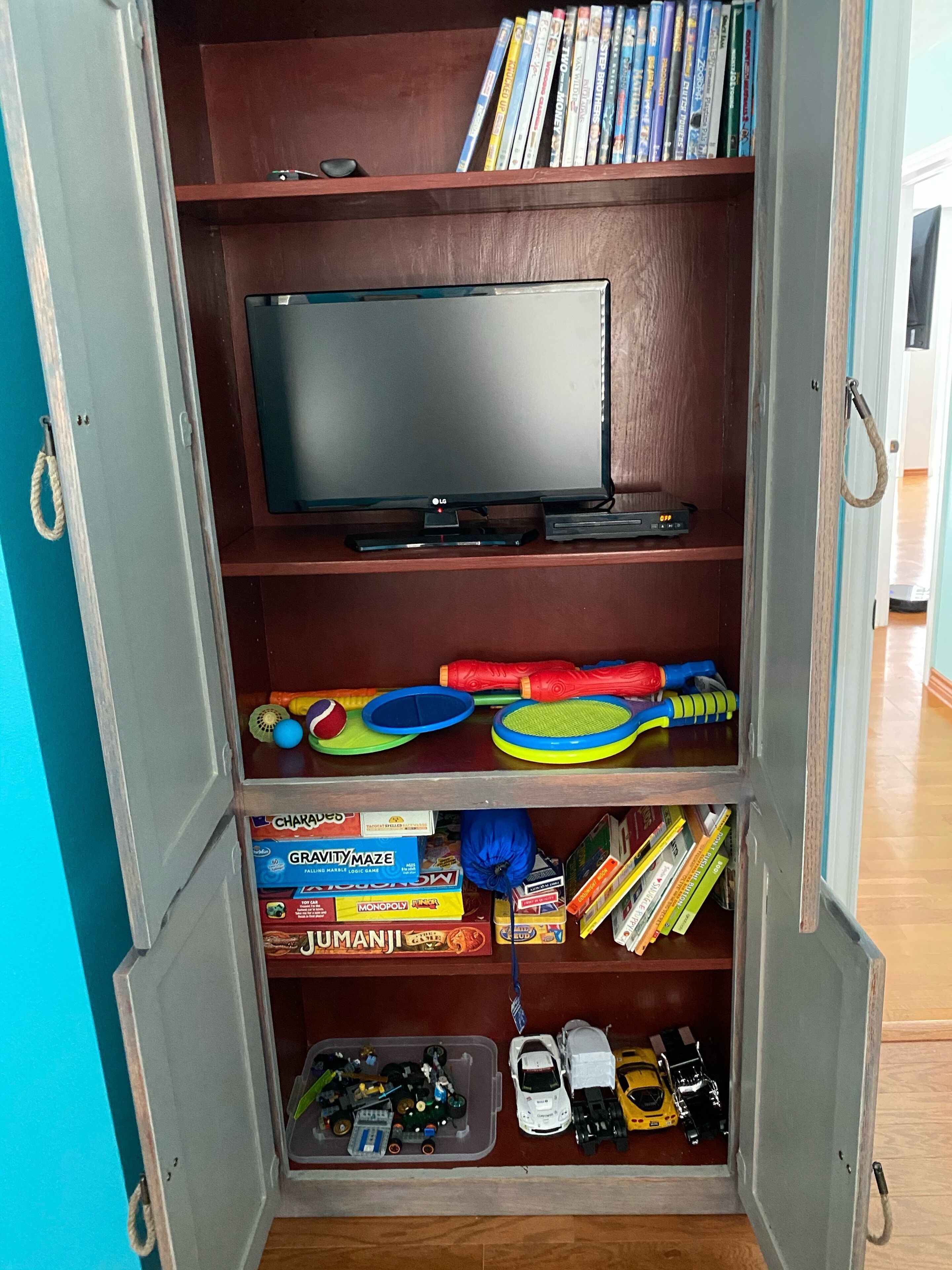 A room with a television on a shelf, a collection of board games, and a toy car display.
