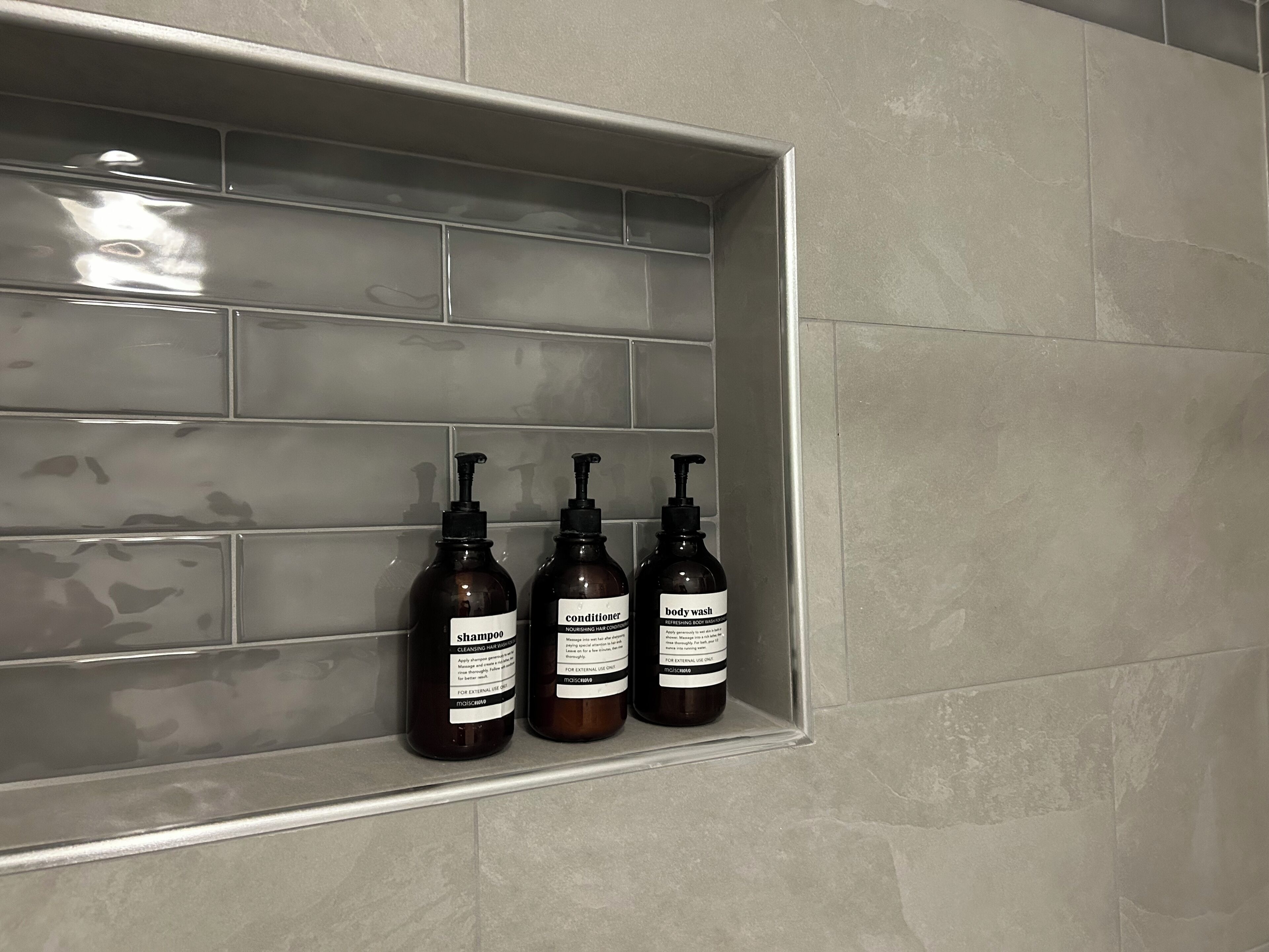 Ein Badezimmer mit gefliesten Wänden und einem Regal mit drei Flaschen Duschgel und Shampoo.
