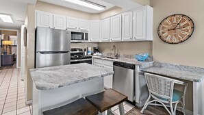 A modern kitchen with white cabinets, stainless steel appliances, a marble countertop, and a wall clock.