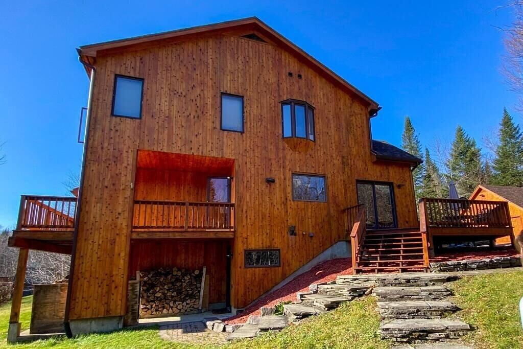 A wooden cabin with a balcony, a staircase, and a log storage area.