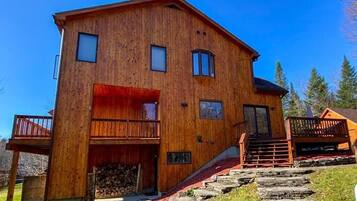 A wooden cabin with a balcony, a staircase, and a log storage area.