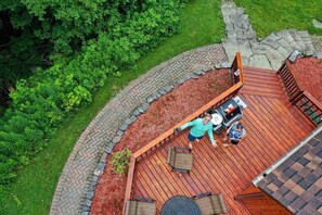 Overzicht van een houten terras met een vuurkuil, zitplaatsen en een pad van stenen.