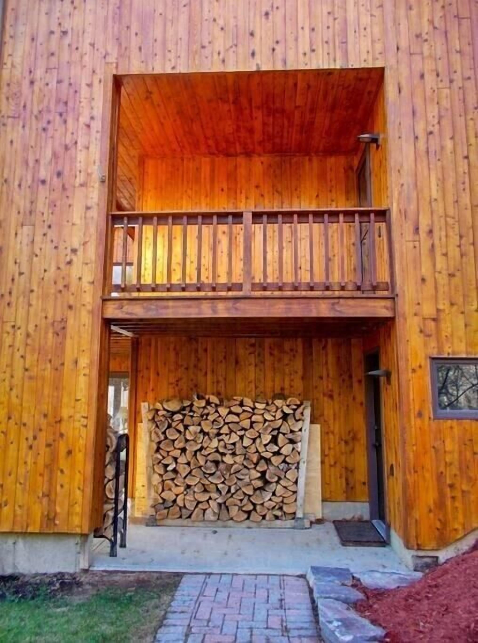 A wooden building with a balcony and a stack of firewood in front.