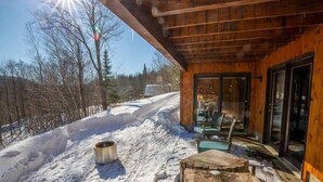 Una cabaña de madera con puerta y ventanas de vidrio, un muelle de madera, y un sendero cubierto de nieve que lleva a la cabaña.